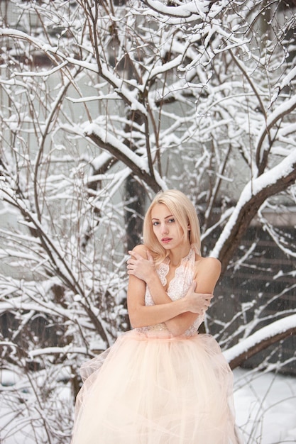 Photo a beautiful young blond woman in a white dress posing in a snowy winter park. soft focus. selective focus