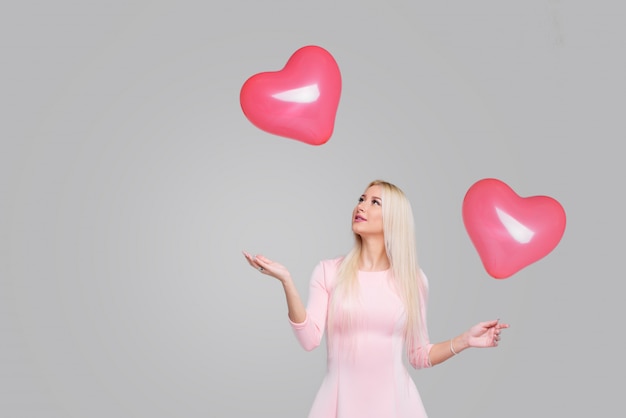 Красивая молодая белокурая женщина с розовым воздушным шаром формы сердца на сером цвете. Женщина на день Святого Валентина. Символ любви - Имидж. Пространство для текста