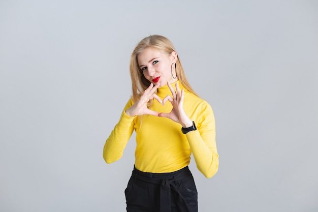Beautiful young blonde girl shows gesture heart with her hands