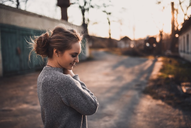 Bello giovane sorriso biondo della ragazza di modello. maglione lavorato a maglia grigio. sul tramonto. ritratto. capelli legati in una crocchia