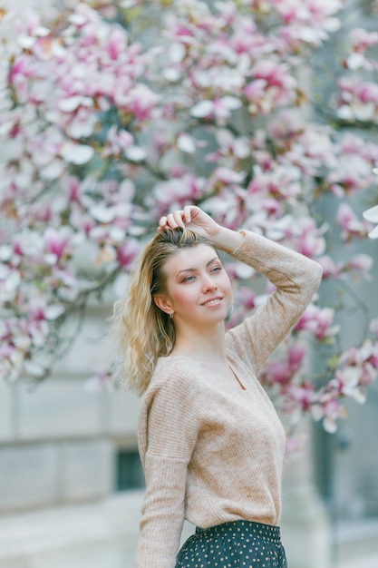 Beautiful young blonde near a blossoming Magnolia tree