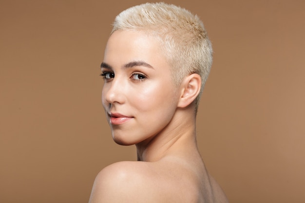 a beautiful young blonde stylish woman with short haircut posing isolated over dark beige wall wall.