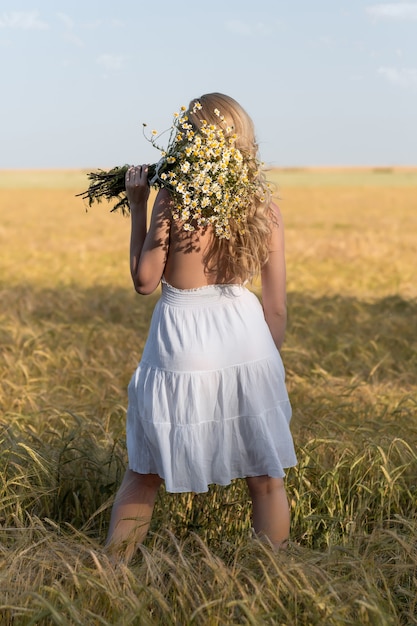 Beautiful young blonde in a wheat field in a white dress in summer