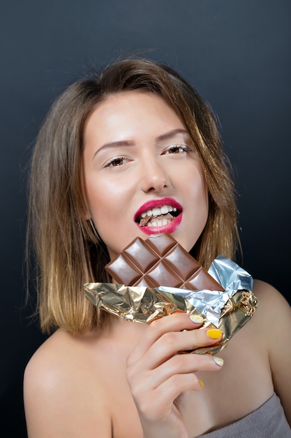 Beautiful young blonde woman eating chocolate bar.