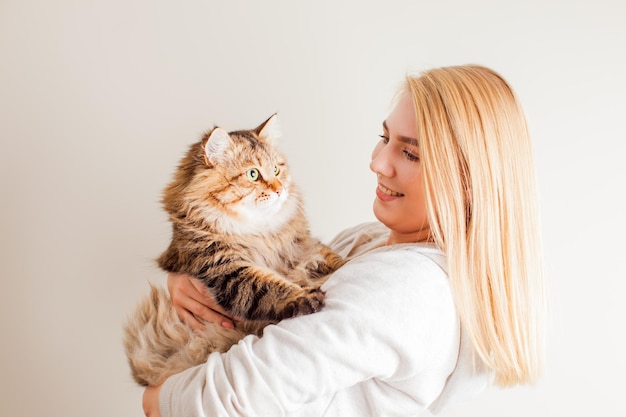 家で休んでいるかわいい猫を保持している美しい若いブロンドの女性