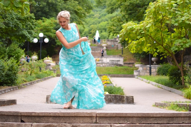 長い緑のドレスを着た美しい若いブロンドの女性が夏の公園で踊っています