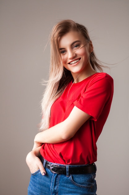 Bella giovane donna bionda in maglietta rossa e jeans che sorride e che posa