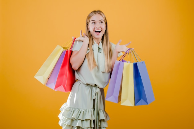 Beautiful young blonde woman smiling with colorful shopping bags isolated over yellow