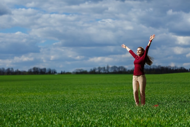 아름 다운 젊은 금발의 여 자가 공원에서 푸른 잔디에 서 있다. 구름과 푸른 하늘입니다. 소녀는 미소를 지으며 좋은 하루를 즐깁니다.