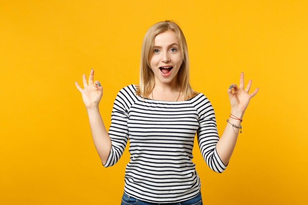 Beautiful young blonde woman in striped clothes hold hands in yoga gesture isolated on bright yellow orange background, studio portrait. People sincere emotions lifestyle concept. Mock up copy space.