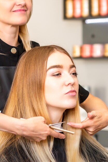 Beautiful young blonde woman with long straight blonde hair getting a haircut at the hairdresser salon