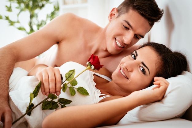 Красивый молодой парень будит своих милых улыбающихся подружек и дарит ей в постели красную розу по утрам.