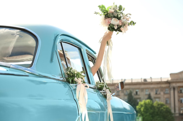 Красивая молодая невеста держит букет в украшенном автомобиле на открытом воздухе