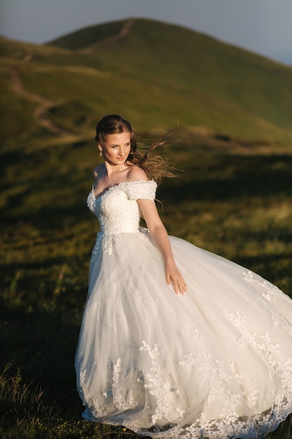 Beautiful young bride stand on the hill in mountais. Windy outdoor. Green hills on background.