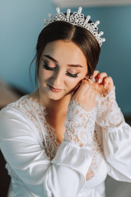 Photo beautiful young bride wearing earrings before wedding ceremony at home the bride in a white robe puts on earrings in her room in the morning