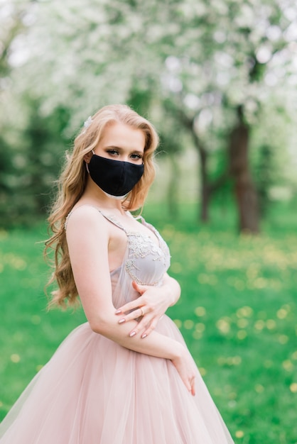 Красивая молодая невеста в свадебном платье и черной медицинской маске