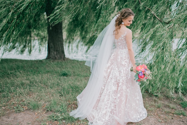 Beautiful young bride in white wedding dress posing outdoor with bouquet of flowers