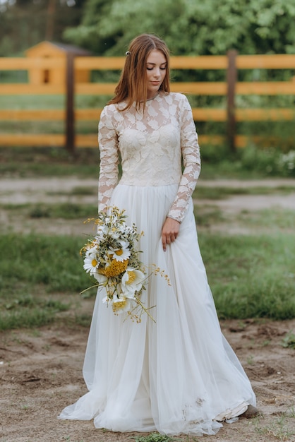 A beautiful young bride with a bouquet of daisies in a field