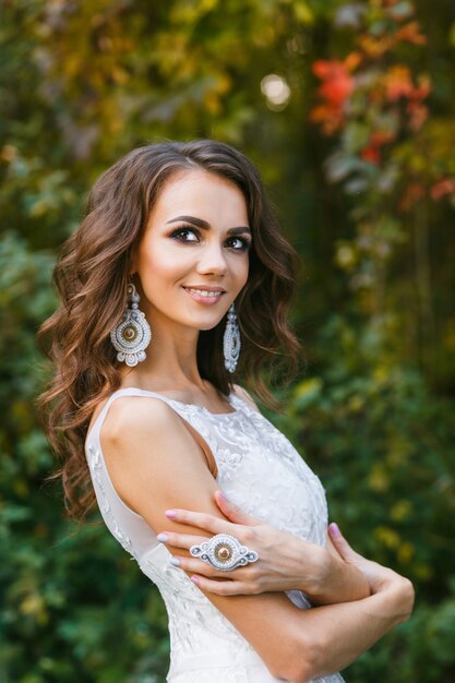 Beautiful young bride with long curly hair posing on foliage background