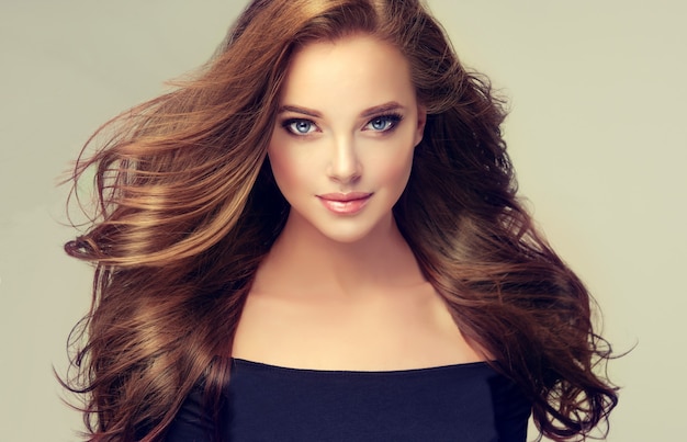 Beautiful young, brown haired woman with voluminous, flying hair. Beautiful model with long, dense, straight hairstyle and vivid makeup. Hairdressing art, hair care and beauty products. 