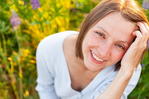 Beautiful young brunete woman resting on summer field with blooming wild flowers green background