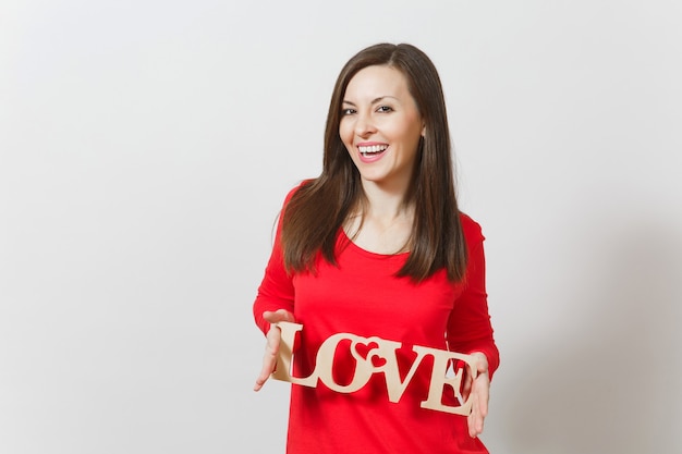 Beautiful young brunette fun smiling woman in red casual clothes holding wooden word love on white background. Copy space for advertisement. St. Valentine's Day or International Women's Day concept.