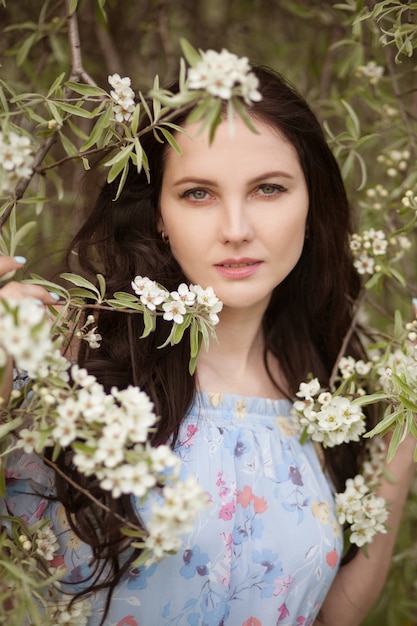 Bella giovane ragazza castana in vestito blu che posa in un giardino di fioritura