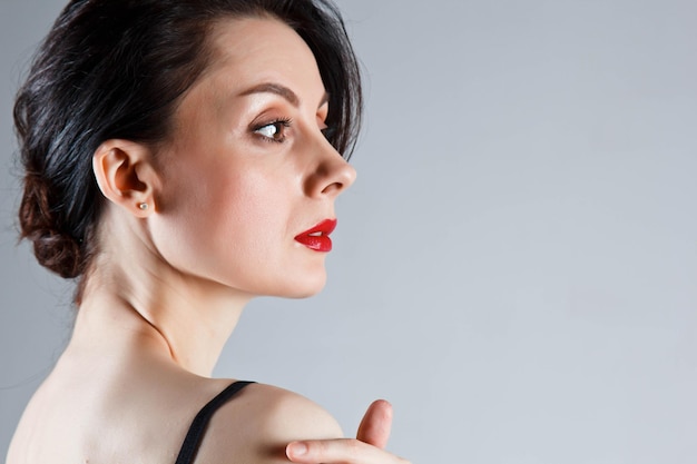 Beautiful young brunette girl with a bare back on a gray background the concept of femininity and tenderness cosmetology