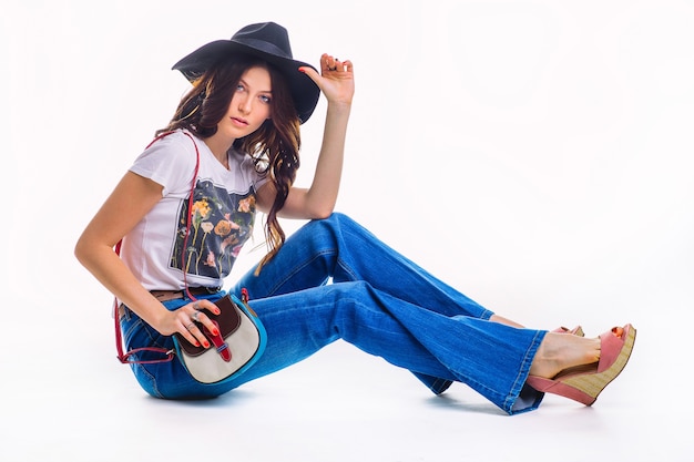 Beautiful young brunette in jeans bell bottom white t-shirt and black hat ,sitting on the floor