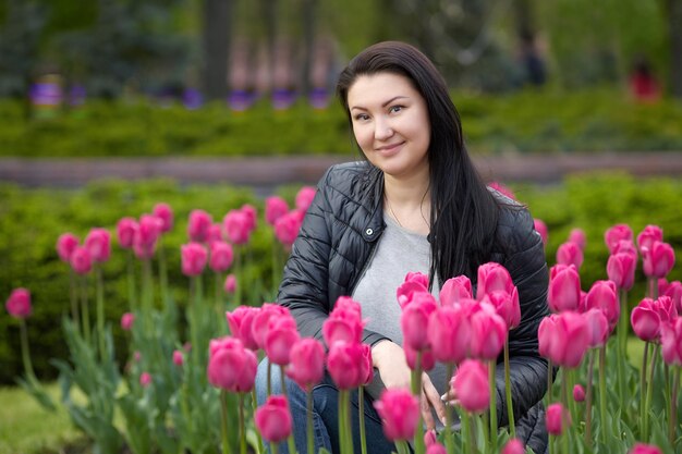 Beautiful young brunette sits in the park surrounded by tulips High quality photo