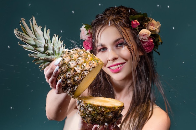 A beautiful young brunette with bright blue eyes in a hawaiian image with a fresh cut pineapple in h...