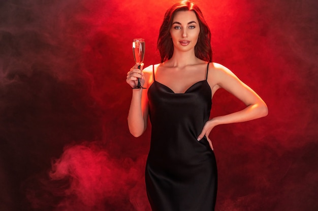 Beautiful young brunette woman in black dress holds glass of champagne party time holiday concept