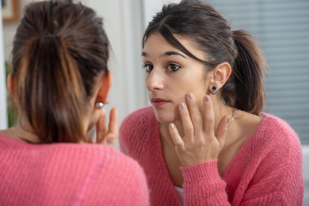 Beautiful young brunette woman looking at herself in the mirror