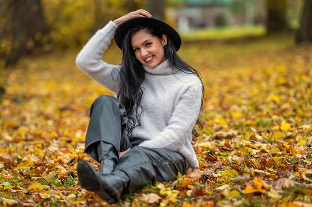 Beautiful young brunette woman in a white sweater and black hat in autumn park