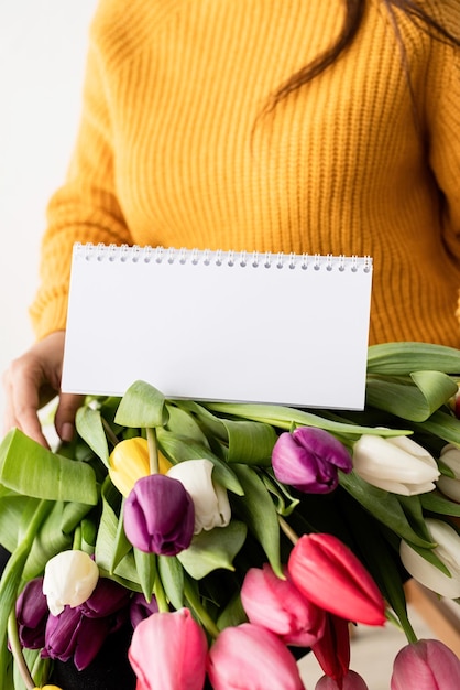 Foto bella giovane donna bruna con un bouquet di tulipani rosa freschi e un calendario vuoto per il mock up