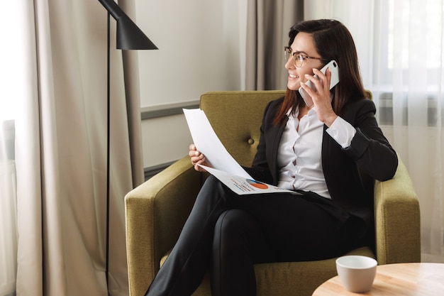 beautiful young business woman in formal wear clothes indoors at home talking by mobile phone work with documents.