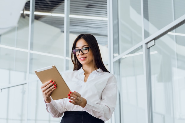 大企業の建物で彼女のタブレットを見て美しい若いビジネス女性