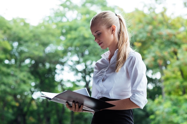 Beautiful young business woman looking through documents while standing outdoos