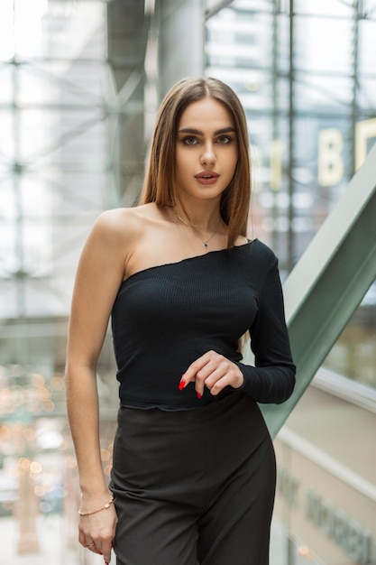 Beautiful young business woman model in a black top and trousers in a glass office building