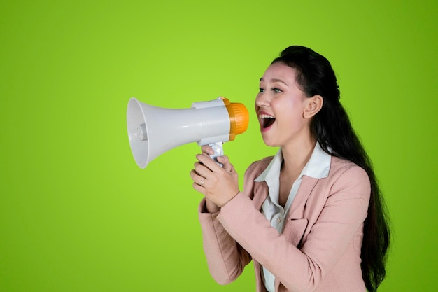 Beautiful young business woman speaking with a megaphone in the studio over green screen background