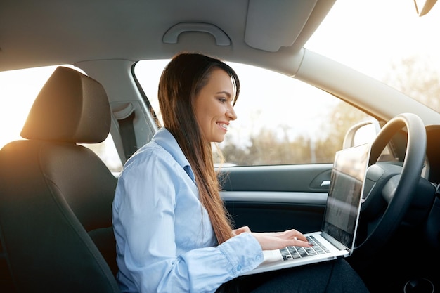 Beautiful young business woman using laptop and phone in the car