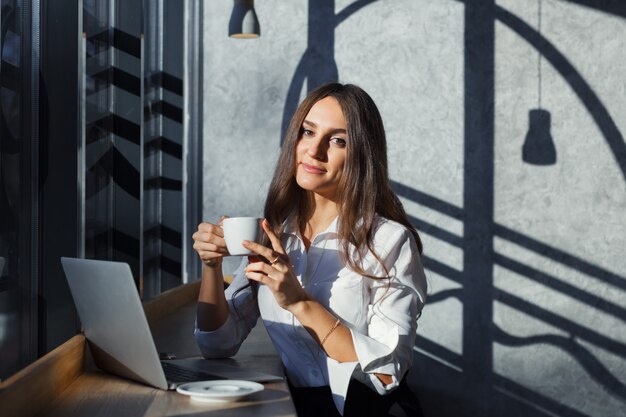 Bella giovane donna d'affari in camicetta bianca utilizzando laptop e smartphone