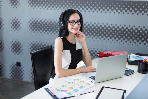 Beautiful young businesswoman in black dress with headphones and glasses