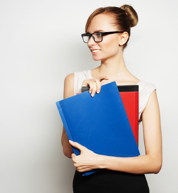 Beautiful young businesswoman holding folders while standing against grey background