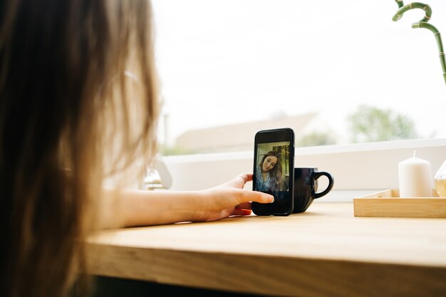 beautiful young caucasian female drinking coffee in kitchen while browsing on cell