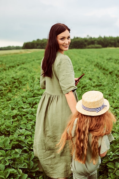 Beautiful young caucasian mother with her daughter in a linen dress with a basket of strawberries gathers a new crop