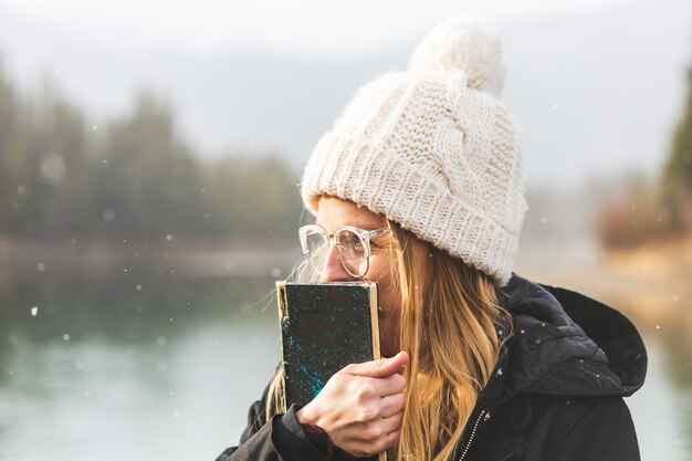 Photo beautiful young caucasian student woman reading a book in winter outside traveler girl smiling having fun under the snow in a sunny day