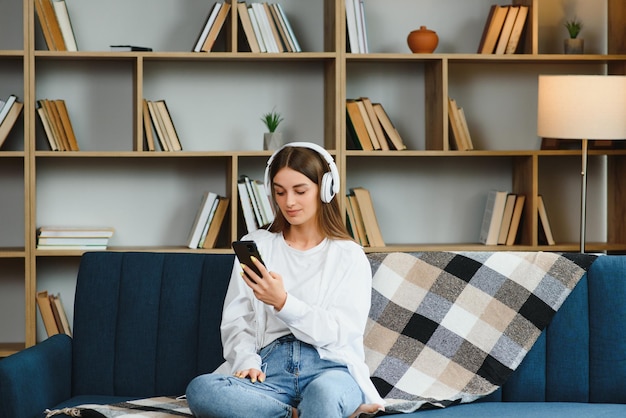 Beautiful young caucasian woman in casual clothing enjoying music and smiling while resting at home Young woman with headphones using laptop at home