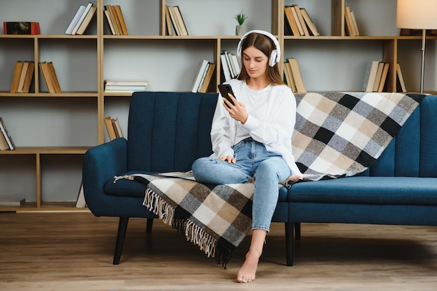 Beautiful young caucasian woman in casual clothing enjoying music and smiling while resting at home Young woman with headphones using laptop at home