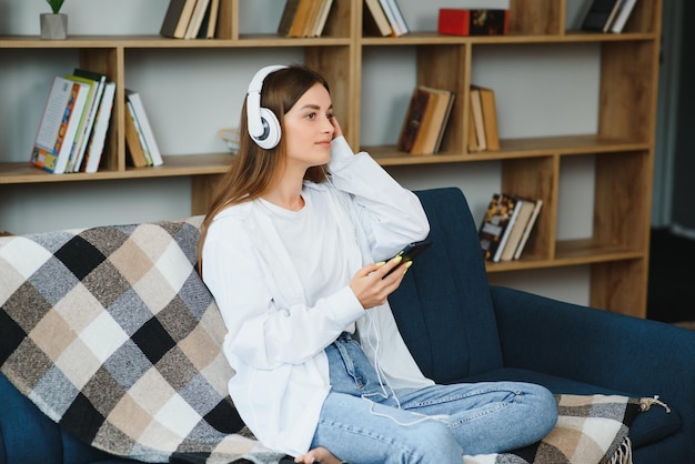 Beautiful young caucasian woman in casual clothing enjoying music and smiling while resting at home Young woman with headphones using laptop at home